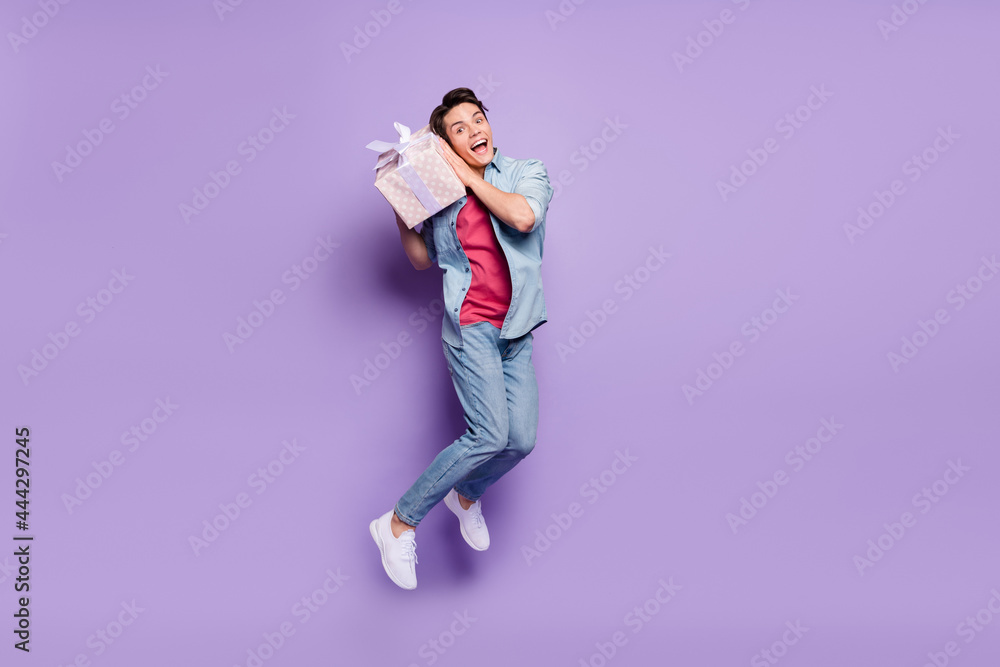 Full size profile side photo of young guy happy smile jump up shake gift box get isolated over purple color background Full size profile side photo of young guy happy smile jump up shake gift box get isolated over purple color background
