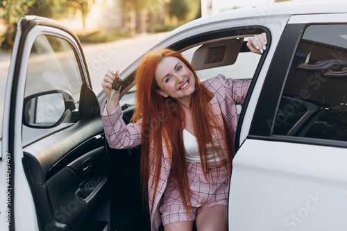 Woman bought first car. Joyful female sitting in new car and shows keys.