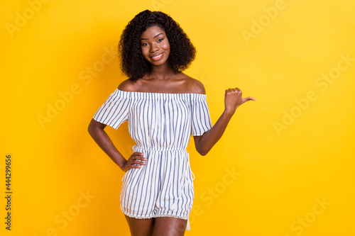 Photo of shiny pretty dark skin lady dressed white clothes pointing thumb up empty space isolated yellow color background