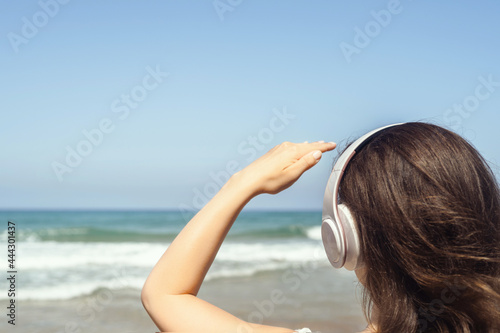 Alone woman on a beach in headphones listen music looking on the sea. Female relaxation at summer vacation. Back view