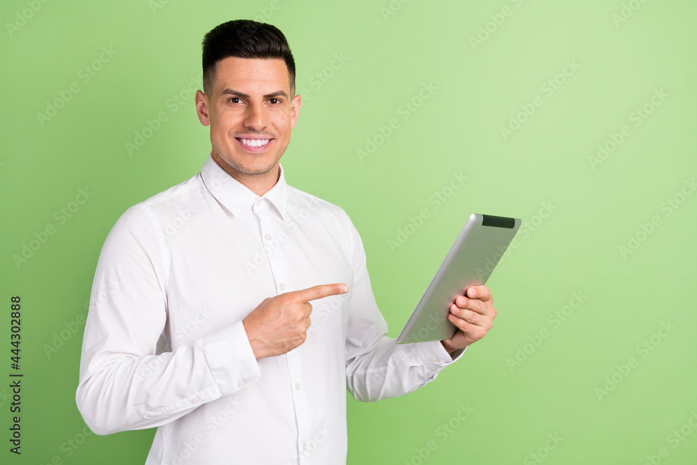 Photo of charming pretty young gentleman wear white shirt smiling pointing modern gadget isolated green color background Photo of charming pretty young gentleman wear white shirt smiling pointing modern gadget isolated green color background