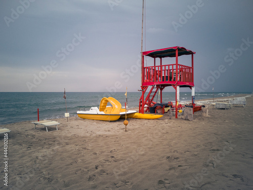 Fototapeta Naklejka Na Ścianę i Meble -  Desolate beach in Viareggio with a lifeguard facility and a pedal boat. The sky is cloudy and ready for a storm