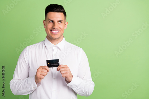Photo of sweet charming gentleman wear white shirt smiling holding bank card looking empty space isolated green color background © deagreez