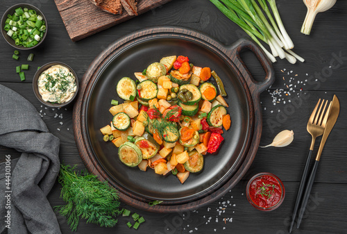 Fried vegetables, fresh herbs and sauces on a black background. Top view.