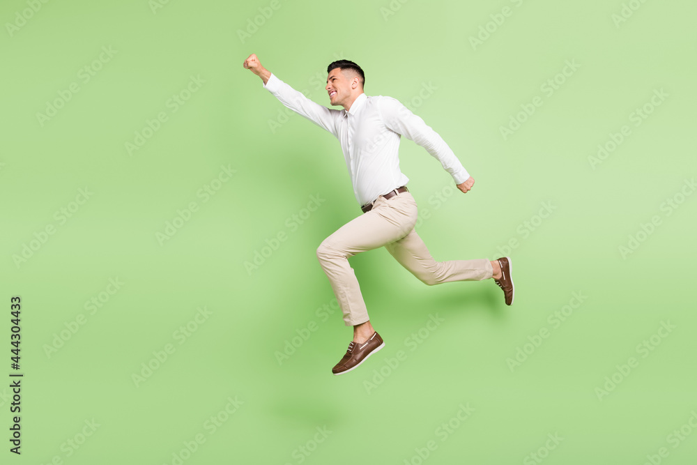 Full length photo of sweet attractive young guy dressed white shirt running fast jumping empty space isolated green color background Full length photo of sweet attractive young guy dressed white shirt running fast jumping empty space isolated green color background