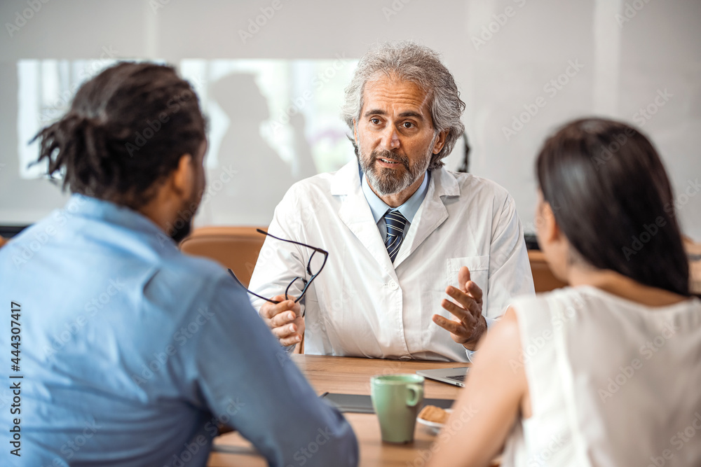 Obraz premium Senior healthcare worker discussing with couple. Male doctor is showing digital tablet to man and woman. They are sitting in hospital. Consultation In Doctors Office