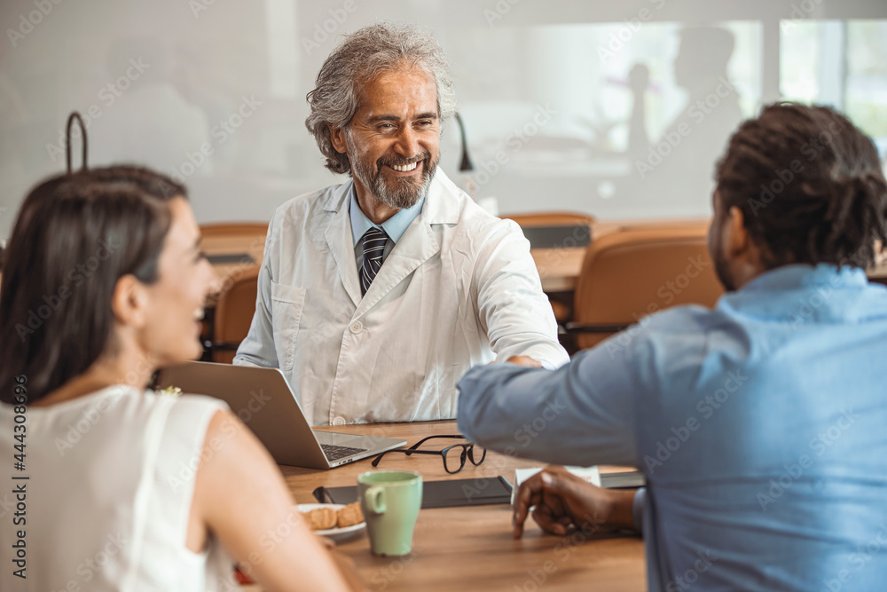 Obraz premium Couple patients consulting with male medical doctor in hospital room. Pregnant woman and her husband at consultation with male doctor in doctors office. A photo of happy male doctor shaking hands 