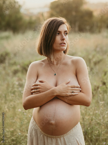 Topless serene pregnant woman covering breast in field photo