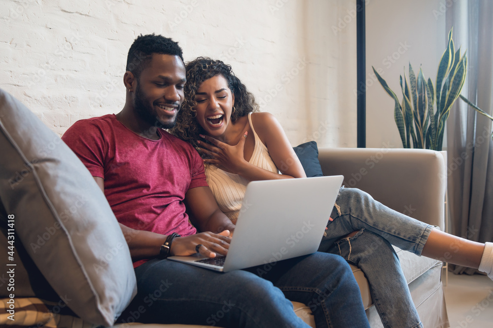 Couple using a laptop while sitting on a couch at home. Couple using a laptop while sitting on a couch at home.