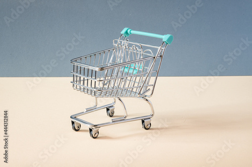 SMALL TOY OF A SHOPPING CART ON BLUE BACKGROUND AND YELLOW FLOOR