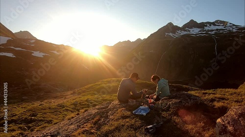 A couple camping in the Austrian Alps near Schladming. They are preparing their meal with the sun setting behind the high mountain peaks. Some snow in the higher parts. Camping in the wilderness. Free