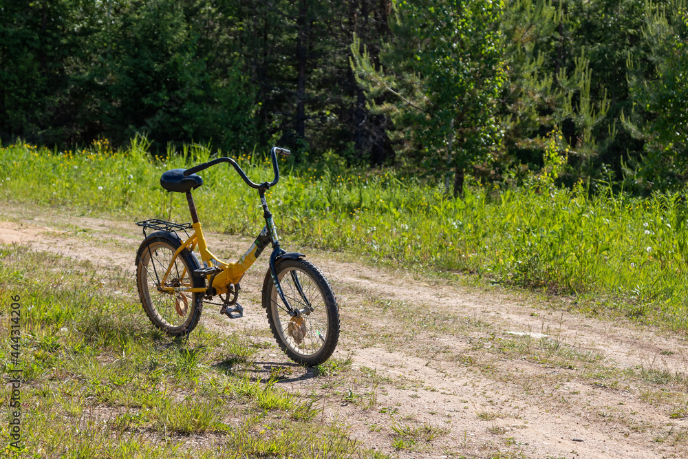 bicycle with a yellow frame stands on a country village road