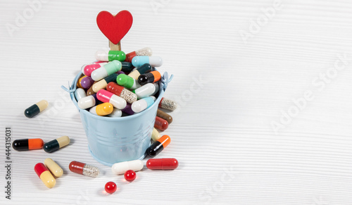 A small bucket of pills with a clothespin with a heart attached on a white table