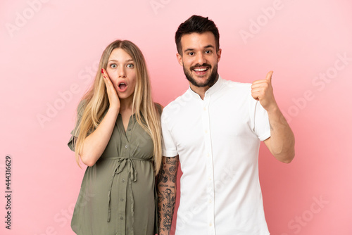 Pregnant woman and man over isolated pink background pointing finger to the side and presenting a product