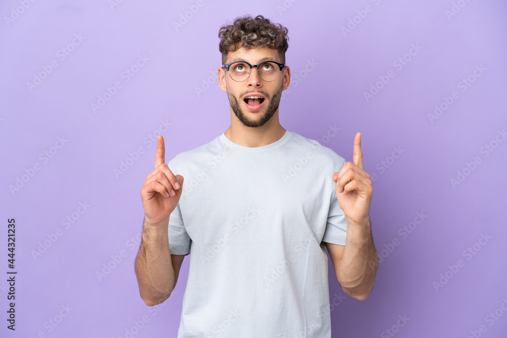 Delivery caucasian man isolated on purple background surprised and pointing up Delivery caucasian man isolated on purple background surprised and pointing up