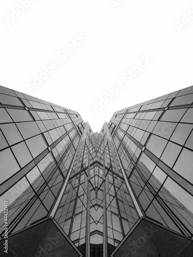 Black and white shot of a tall glassed business building facing the sky with mirroring glass windows and metallic frames