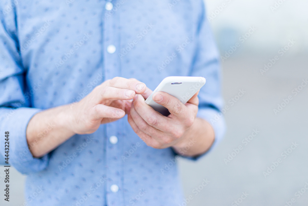 A man in a shirt uses a smartphone in the summer in the city A man in a shirt uses a smartphone in the summer in the city
