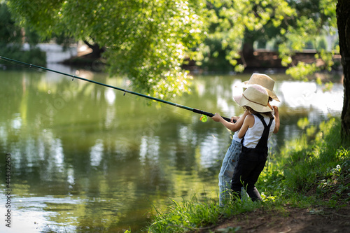 A boy and a girl with curly hair in straw hats stand with a fishing rod by the pond. Children fishing on a summer day.