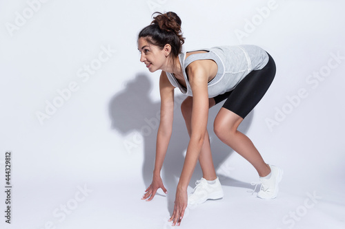 Young woman in sportswear at a low start. Beautiful slender brunette. White background. Active lifestyle.