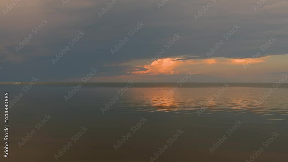 Large lake or ocean at sunset with small waves reflects clouds and the sky. A small boat moves in from the left side.
Large lake or ocean at sunset with small waves reflects clouds and the sky. A small boat moves in from the left side.