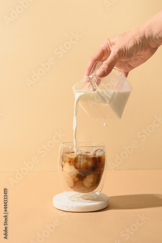 Принти на полотні Pouring milk in coffee with ice cube on modern beige background