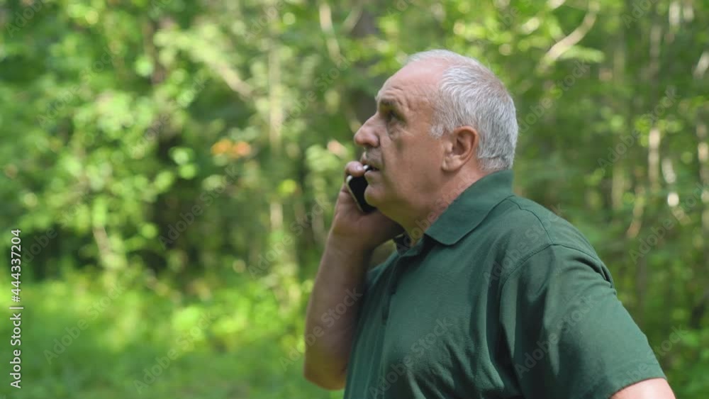 Senior adult Caucasian male using his phone in the forest on a misty morning. Man is talking by Phone. Happy retirement concept Senior adult Caucasian male using his phone in the forest on a misty morning. Man is talking by Phone. Happy retirement concept