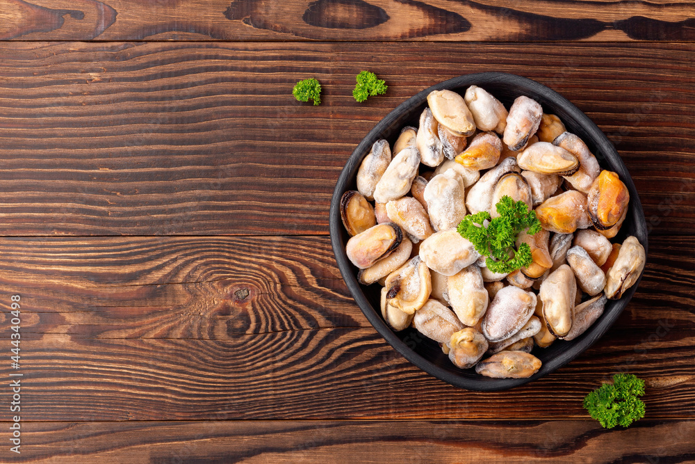 Fototapeta premium Frozen seafood with green parsley in a black dish on wooden background, top view with empty space.