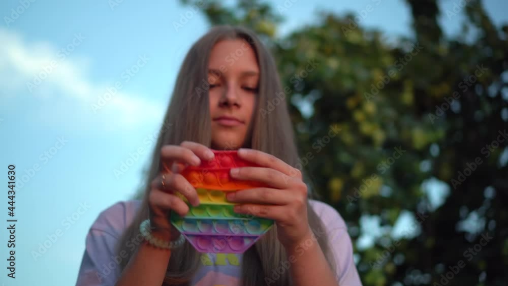 A girl with long hair plays popit in nature. Pop it is a popular silicone toy for children. A girl with long hair plays popit in nature. Pop it is a popular silicone toy for children.