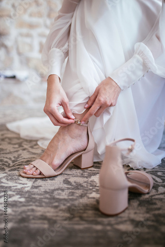 Closeup of a bride in white lace wedding dress put on her shoes. Beautiful stylish wedding. Modern bridal style. 