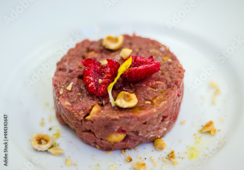 raw meat tartare macro with raspberry and nuts on white plate
