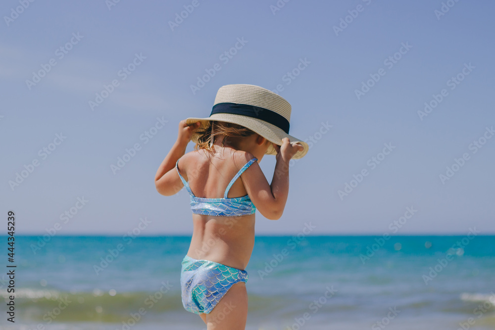 little beautiful girl walks on the sea on the beach in a mermaid swimsuit and a straw hat with a ribbon little beautiful girl walks on the sea on the beach in a mermaid swimsuit and a straw hat with a ribbon
