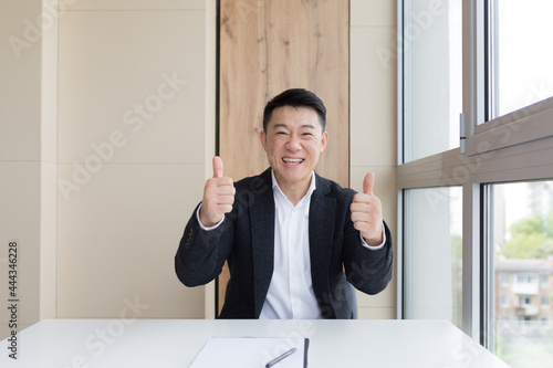 portrait of happy young asian male office worker looking at camera and smiling indoors. Close up of a friendly manager in a formal suit and white shirt sitting at work. business man feeling receiving