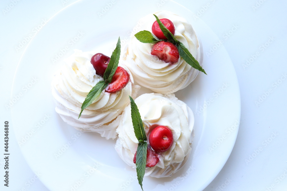 Pavlova's homemade dessert on a white plate.Meringue and cream decorated with strawberries, cherries and mint 