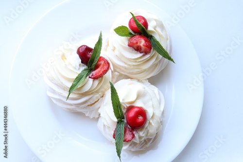 Pavlova's homemade dessert on a white plate.Meringue and cream decorated with strawberries, cherries and mint 