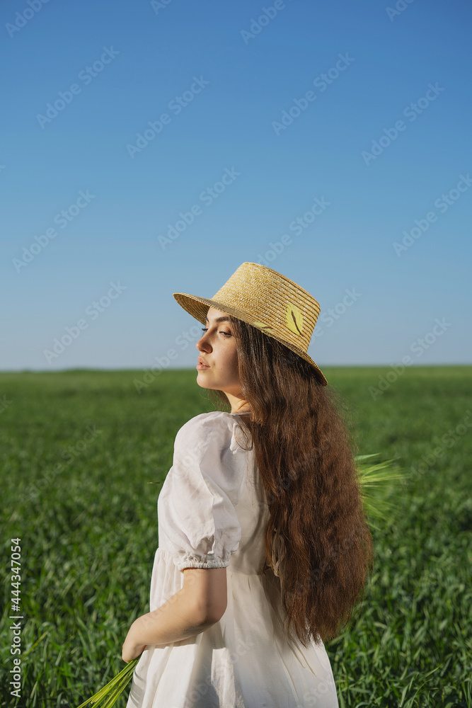 Obraz premium girl in a straw hat and a sundress against the background of a green field and a clear blue sky