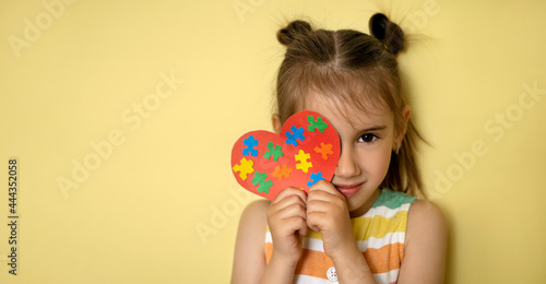A beautiful girl holds a heart with colorful puzzles in her hands  covering one eye. World Autism Awareness Day. Banner