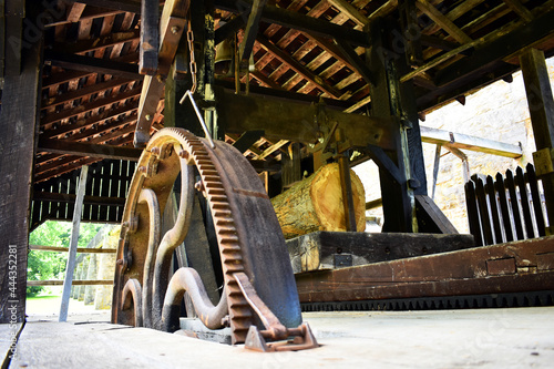 Old fashioned sawmill in operation.  A large metal gear powers the saw working through the log.