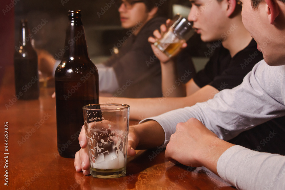 Take detail of a young man clutching a glass while his friends drink beer, at the bar.