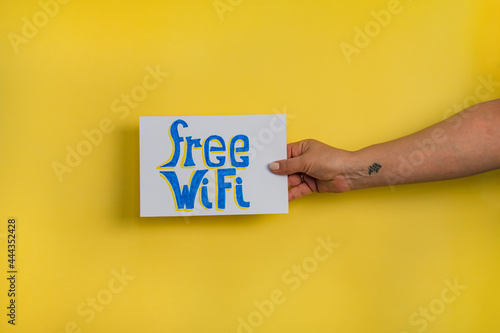 A closeup shot of a woman holding a paper with the word "FREE WIFI" on a yellow background
