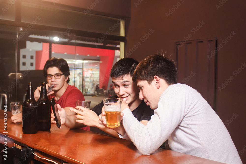 A man showing an image to his friends from his smart phone, while drinking beer at the bar.