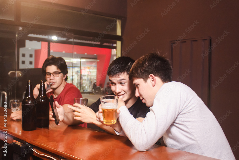 A man showing an image to his friends from his smart phone, while drinking beer at the bar. A man showing an image to his friends from his smart phone, while drinking beer at the bar.