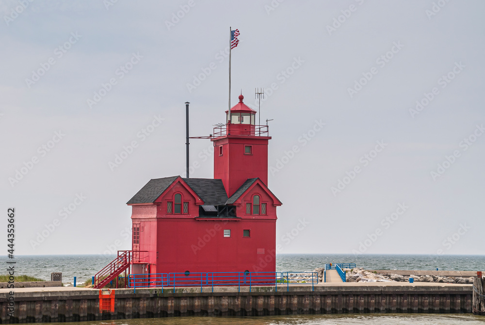 Holland, MI, USA - June 8, 2008: Closeup of red harbor lighthouse at lands end with blue Michigan Lake under light blue sky. American flag on top.