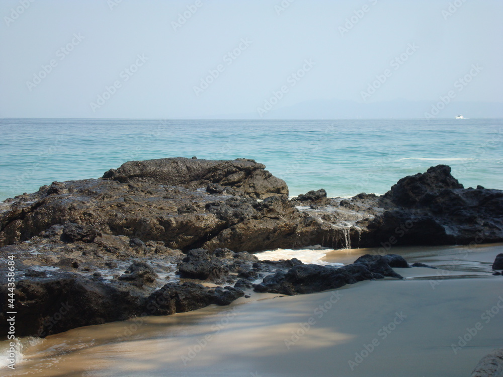 Playa rocosa a la sombra del risco, con horizonte marino 