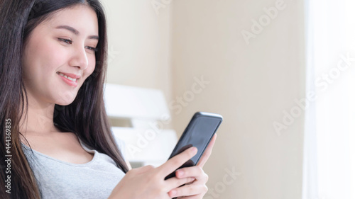 Beautiful cute girl Asian woman playing a smart phone shopping online in white bedroom - lifestyle female online shopping at home concept