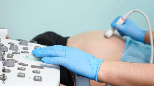 Specialist in gloves turns joystick and presses keys on control panel of ultrasound machine examining pregnant woman in hospital close view