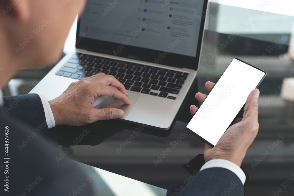Mockup image, business man hand holding black black mobile smart phone working on laptop computer on table at office Mockup image, business man hand holding black black mobile smart phone working on laptop computer on table at office