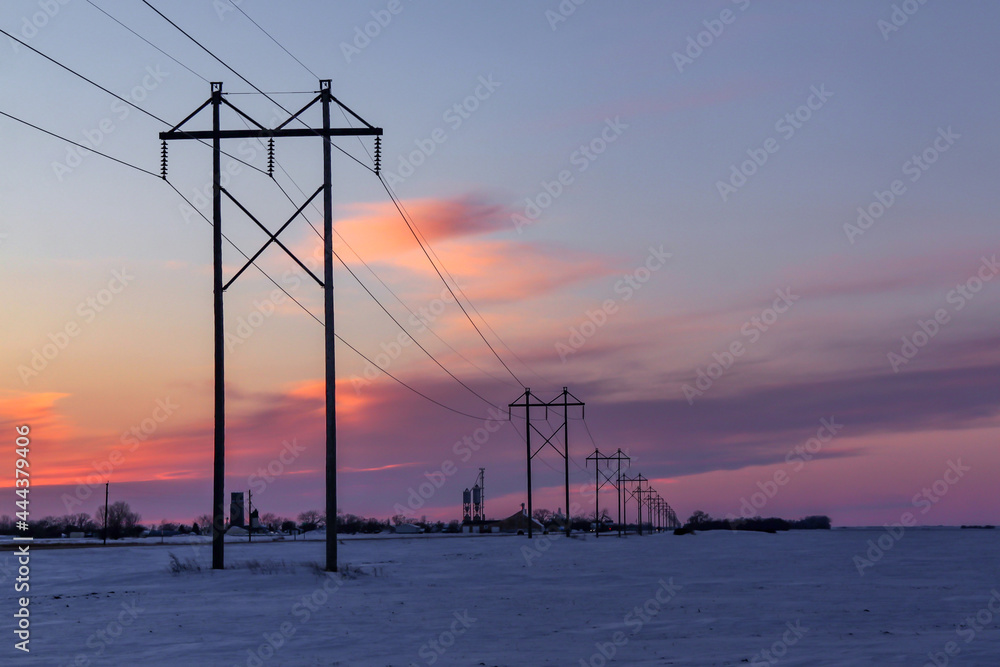 Row of power line poles near a small town at sunset in the Winter in rural Minnesota, USA
