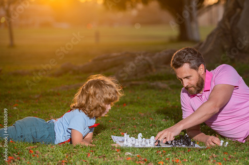 Father and son playing chess spending time together outdoor. Young boy beating a man at chess.