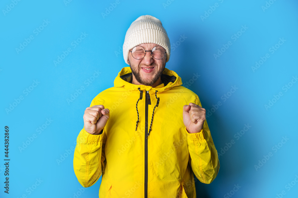 Bearded young man closing his eyes squinting fists clenched on a blue background Bearded young man closing his eyes squinting fists clenched on a blue background