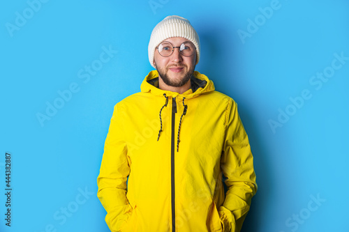 Smiling young man with glasses in a yellow jacket on a blue background © Alex